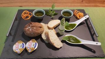 Eine Platte mit Wurstwaren, Brot, Käse und grünen Soßen auf einer Schiefertafel.