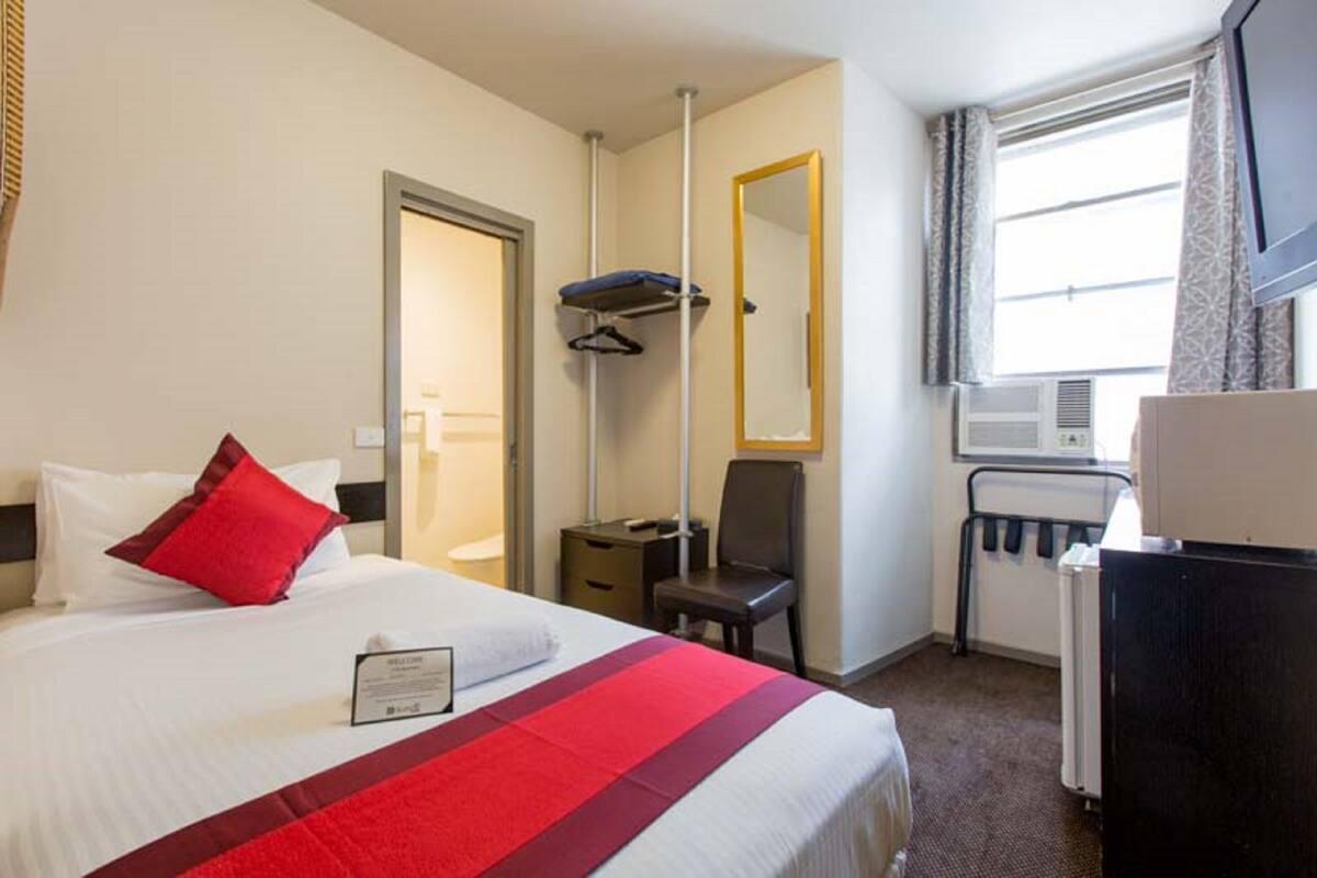 A hotel room with a bed, a desk, a chair, a mirror, and a window.
