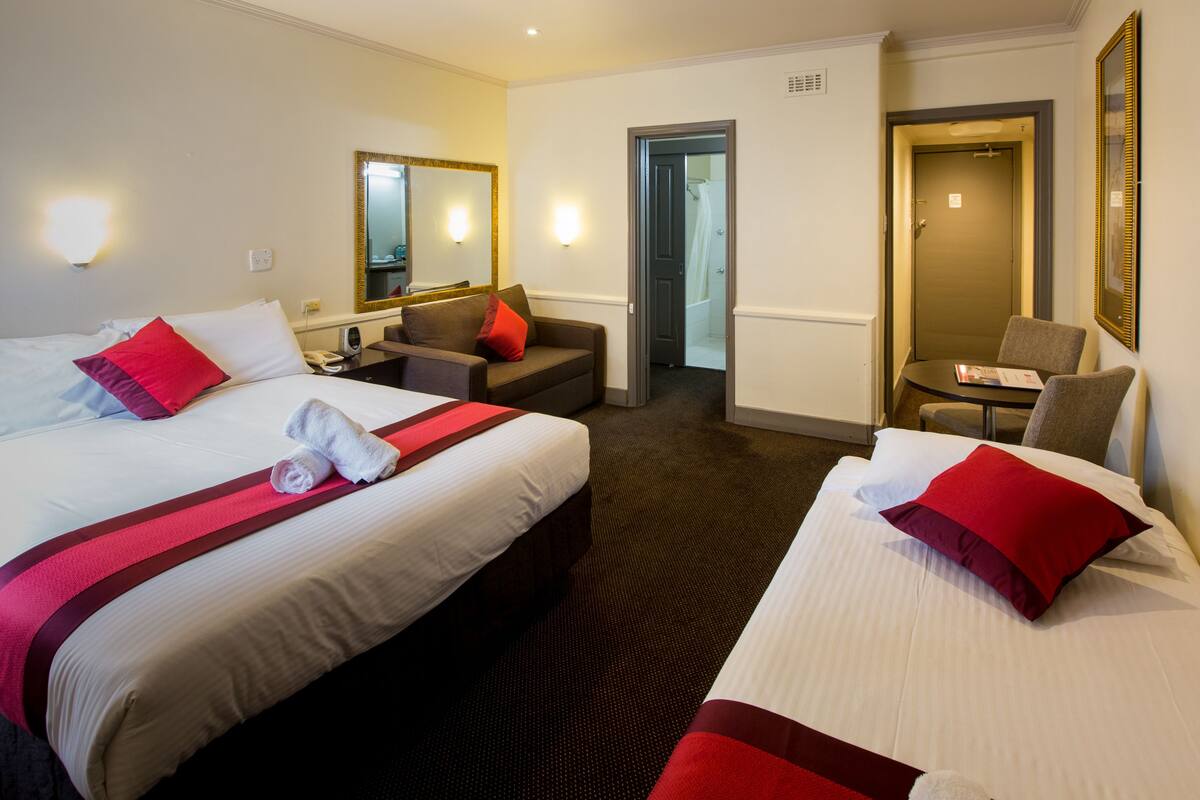 A hotel room with two beds, a desk, a chair, a mirror, and a door leading to a bathroom.