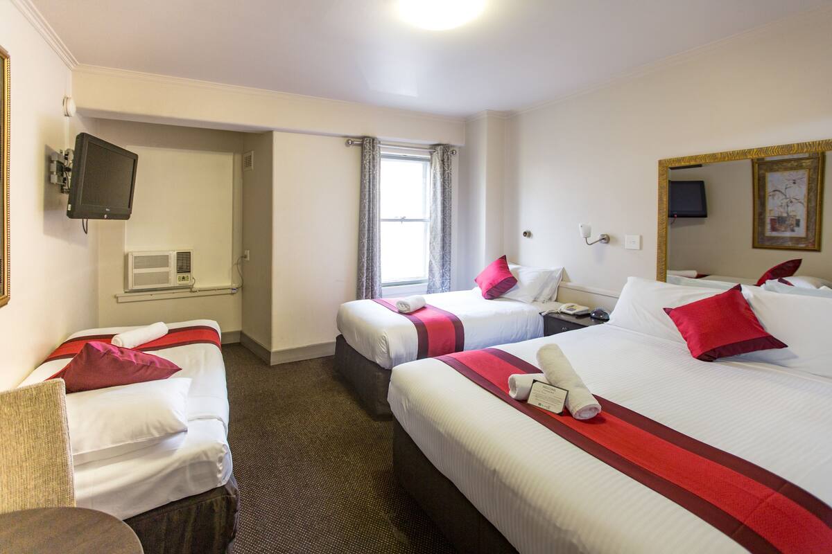 A hotel room with two beds, a TV, a desk, and a window.