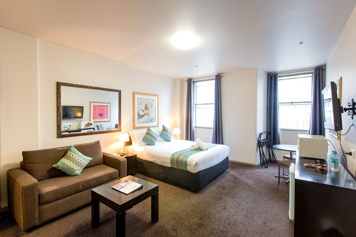 A hotel room with a bed, a sofa, a desk, a chair, a TV, and a window with curtains.