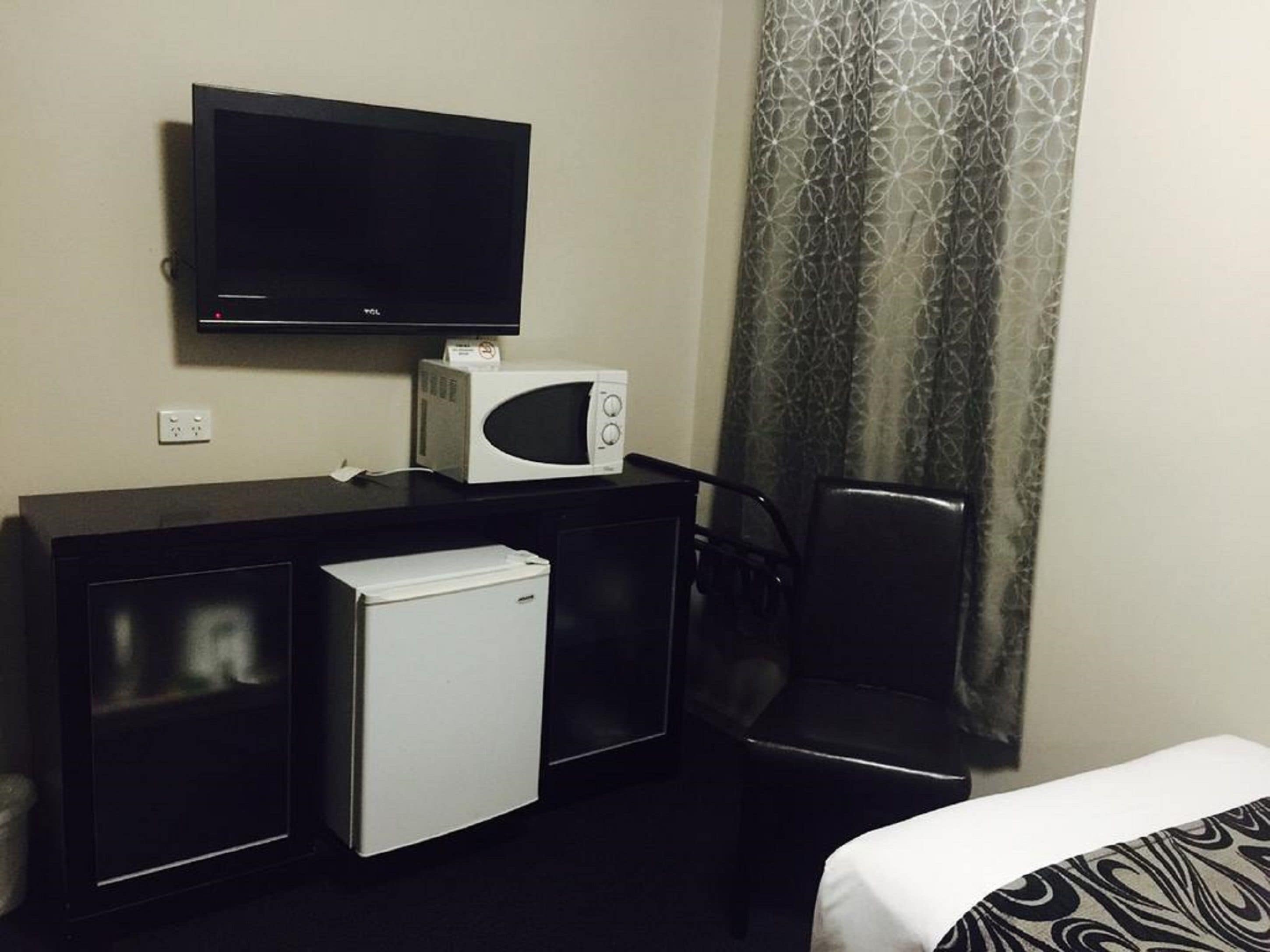 Habitación de hotel con televisión de pantalla plana, microondas, mini refrigerador, un sillón de cuero negro y una cama con ropa de cama estampada.