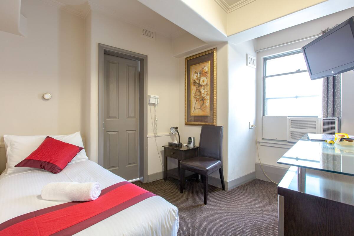 A hotel room with a bed, a desk, a chair, a painting, and a television.