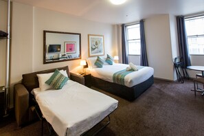 Habitación de hotel con dos camas, un escritorio, una silla, un televisor y obras de arte en las paredes.