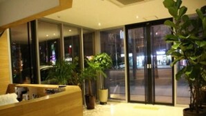 A reception area with a wooden reception desk, potted plants, and large glass doors leading to the street. - Lavilla Hotel (Seoul)