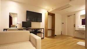A modern hotel room with a sofa, a flat-screen TV, a wooden wardrobe, and a bathroom with a sink and mirror. - Lavilla Hotel (Seoul)