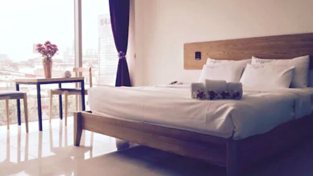 A hotel room with a large bed, a wooden headboard, a small table with a vase of flowers, and a view of the city through large windows. - Lavilla Hotel (Seoul)