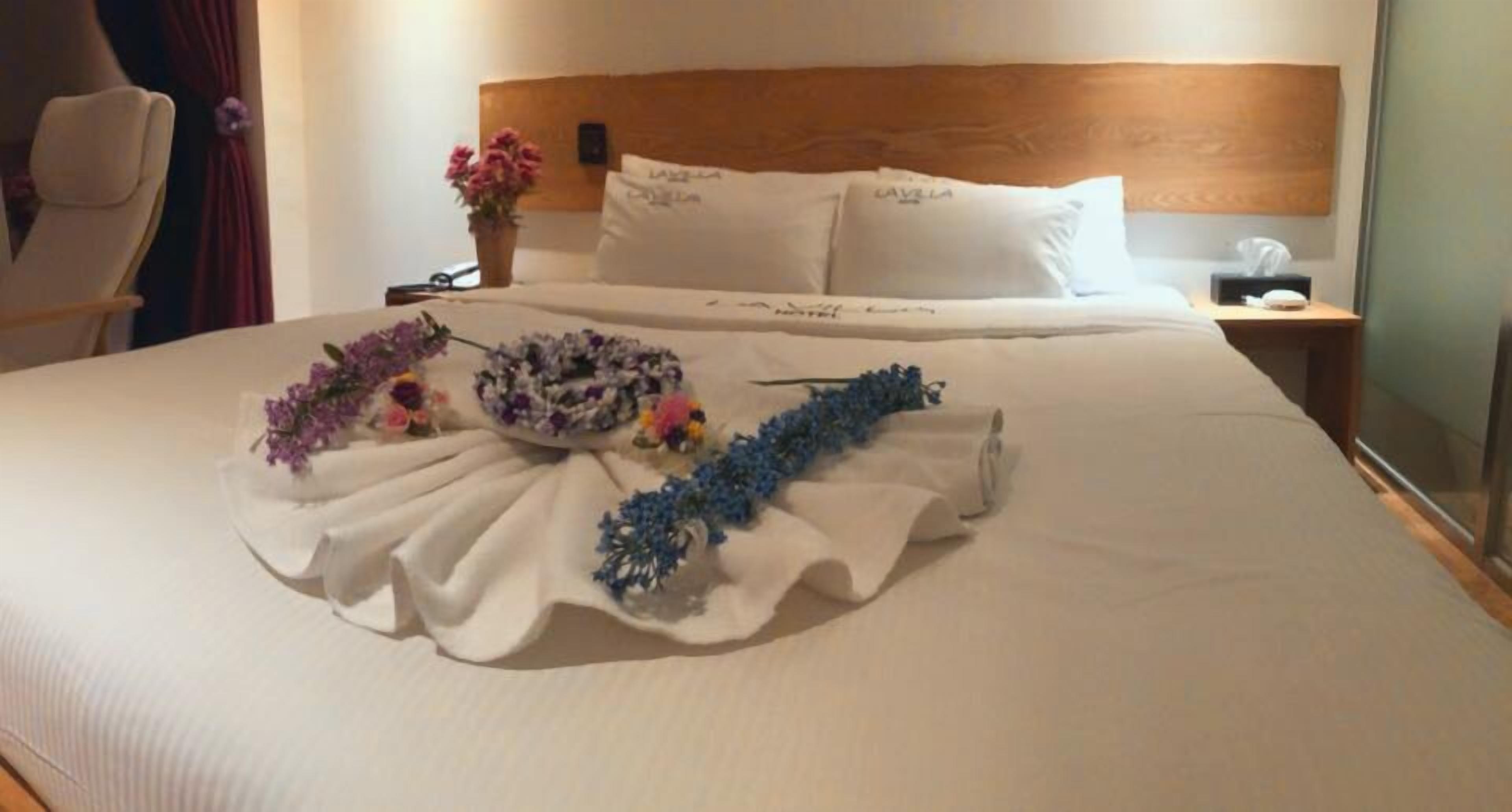 A neatly made bed with white linens, a headboard, and a bedside table with a lamp.