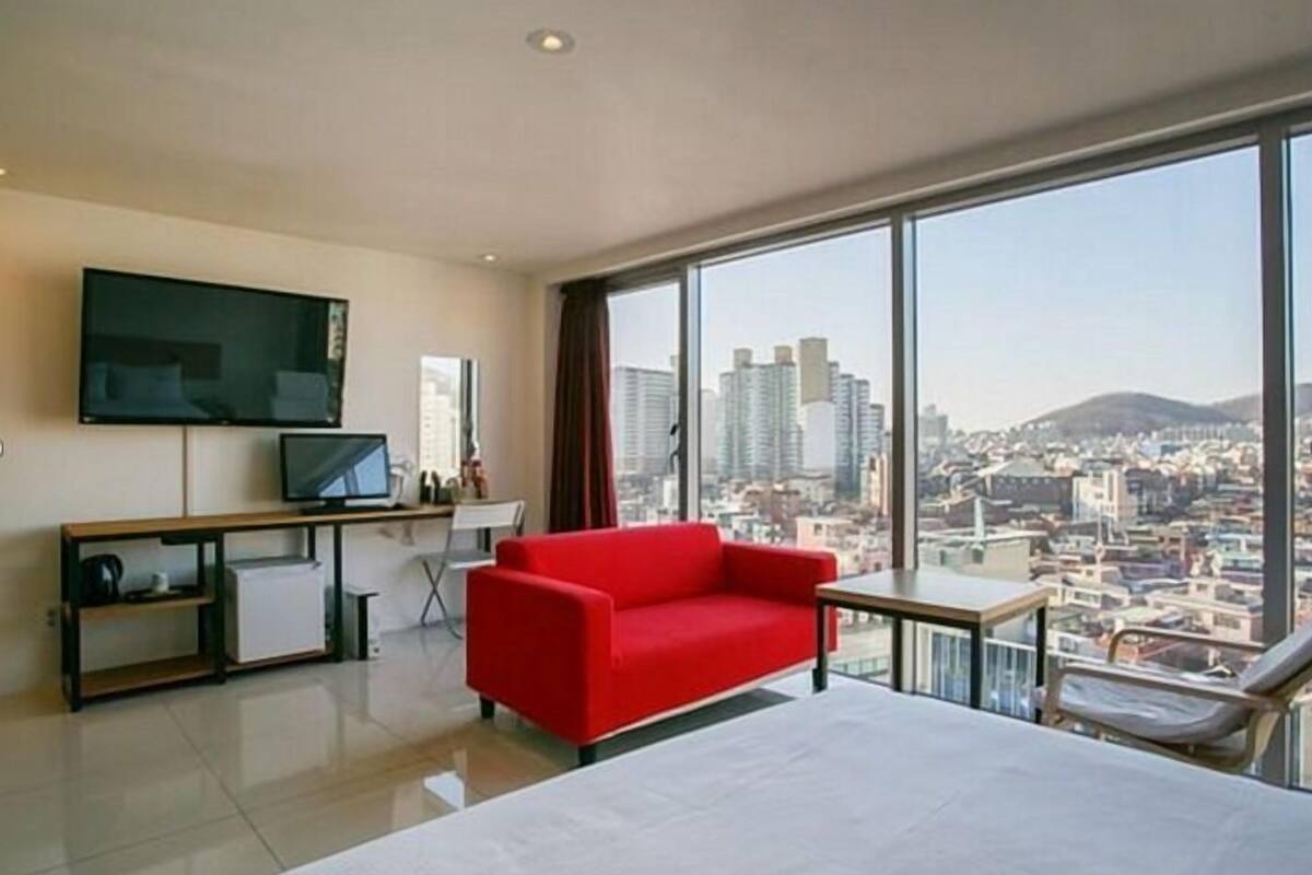 Una habitación de hotel moderna con una cama grande, un sofá rojo, un escritorio con una computadora y un televisor.
