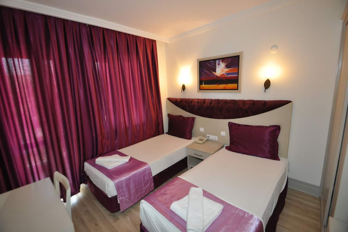 A hotel room with two beds, a desk, a chair, a painting on the wall, and a window with curtains.