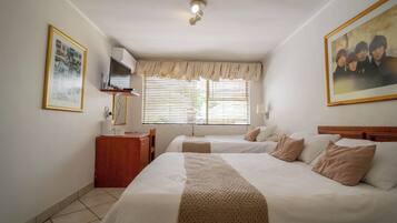 Habitación de hotel con dos camas, un escritorio, una silla, un televisor y una ventana con persianas.