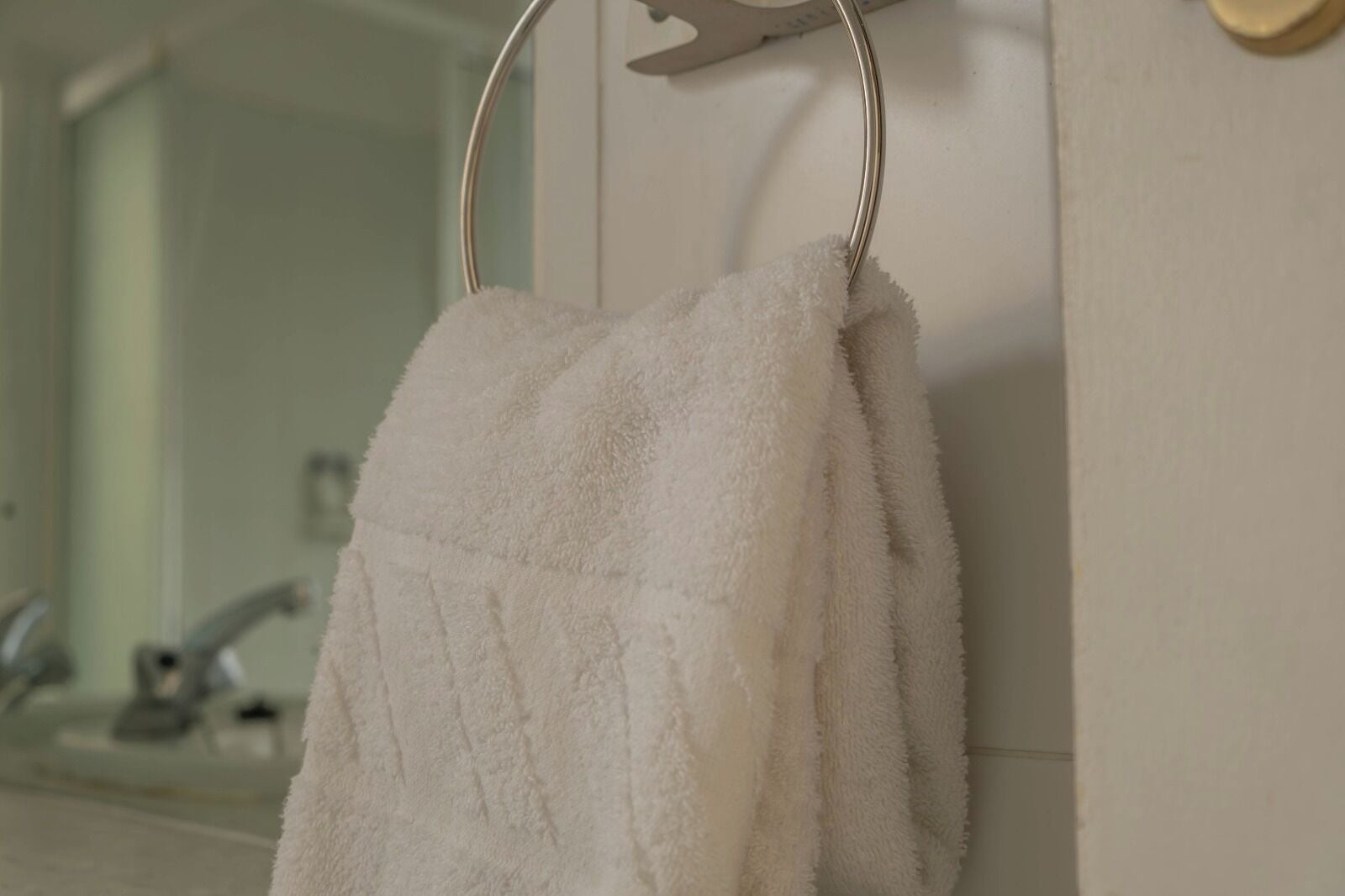 A white towel hanging on a metal towel ring in a bathroom.