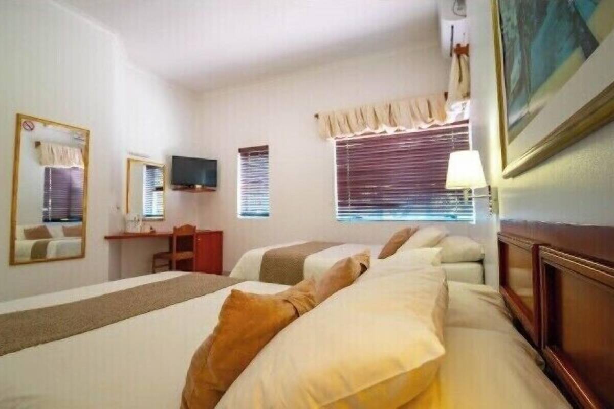 Ein Hotelzimmer mit zwei Betten, einem Schreibtisch, einem Fernseher und einem Fenster mit Jalousien.