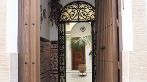 Una puerta de madera con un arco decorativo que da a un pasillo con baldosas estampadas y una planta en maceta.