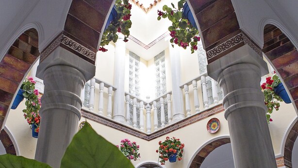 Un interior con techo abovedado, columnas y cestas de flores colgantes.