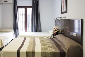 A hotel room with two beds, a large window with curtains, a bedside table with a lamp, and a framed picture on the wall. - Casa de los Faroles (Córdoba)