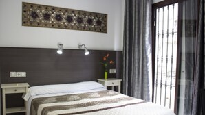 Un dormitorio con cama, mesitas de noche, una lámpara de pared, un adorno en la pared y una ventana con cortinas.