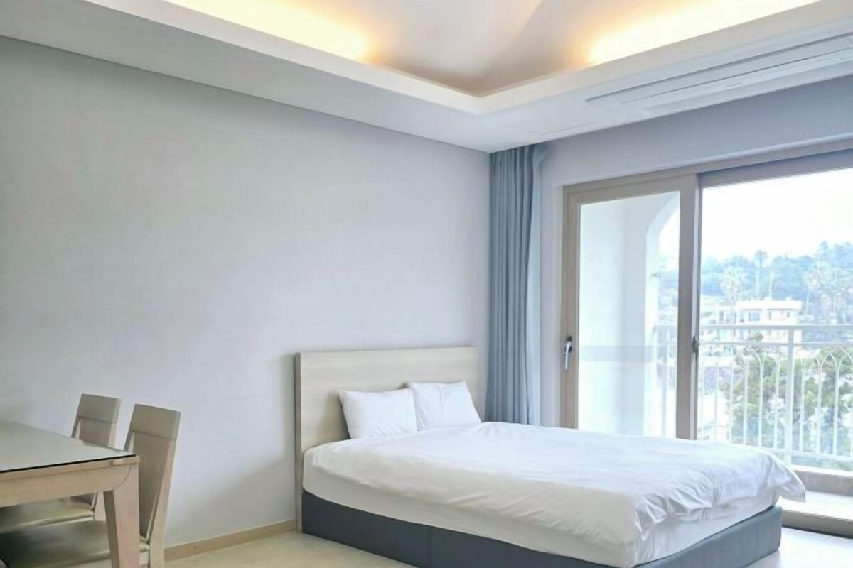 A hotel room with a bed, a dining table, and a view of the city.