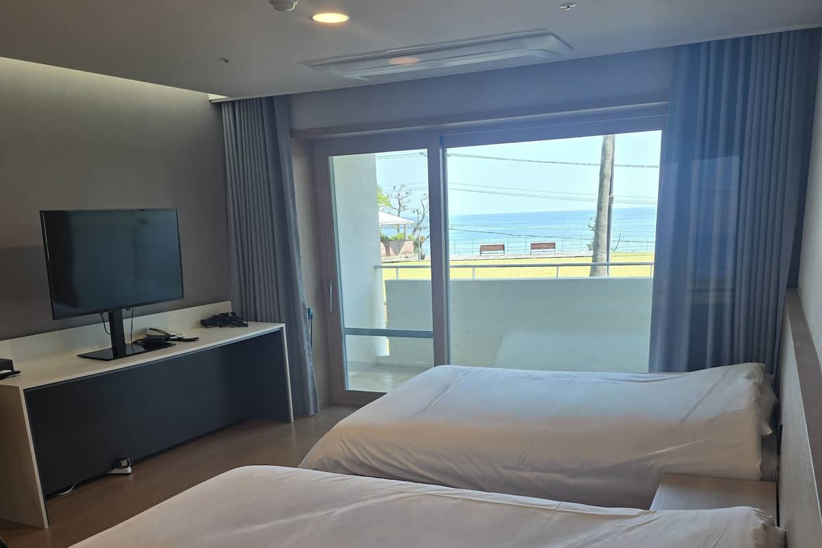 A hotel room with two beds, a TV, and a balcony with a view of the sea.