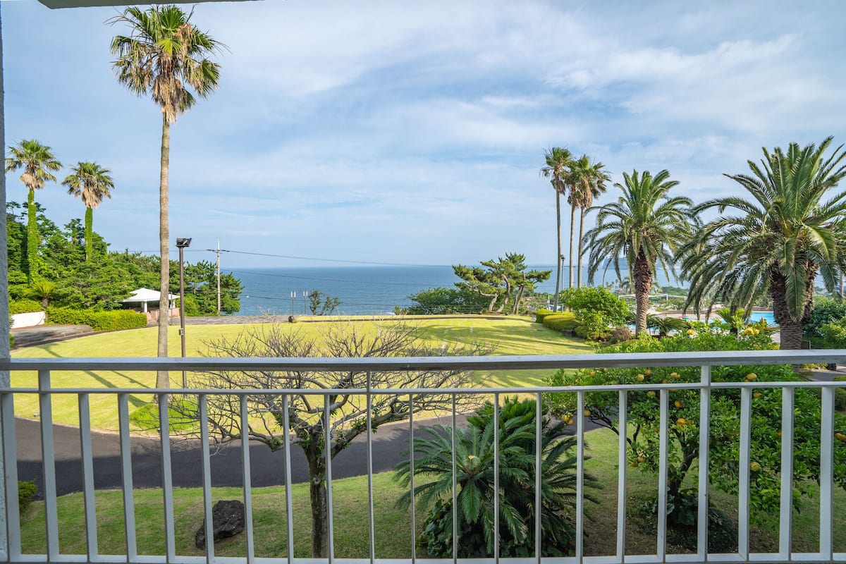 A view from a balcony overlooking a well-maintained lawn with palm trees and a pool area.