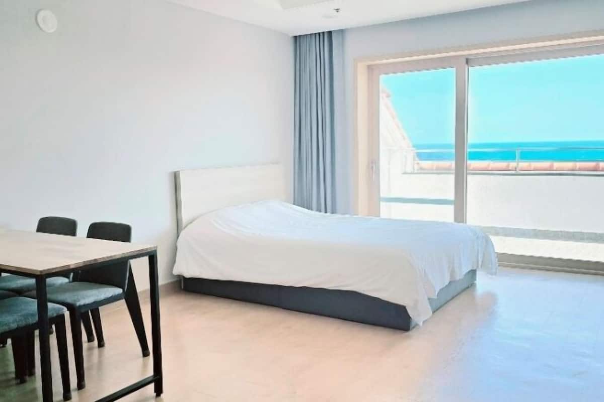 A modern hotel room with a large bed, a dining table with chairs, and a balcony with a view of the ocean.