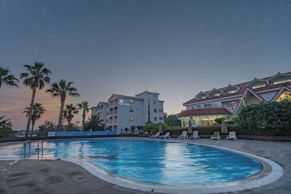 A swimming pool with lounge chairs, palm trees, and buildings with balconies under a starry sky. - Seaore Resort (Seogwipo)