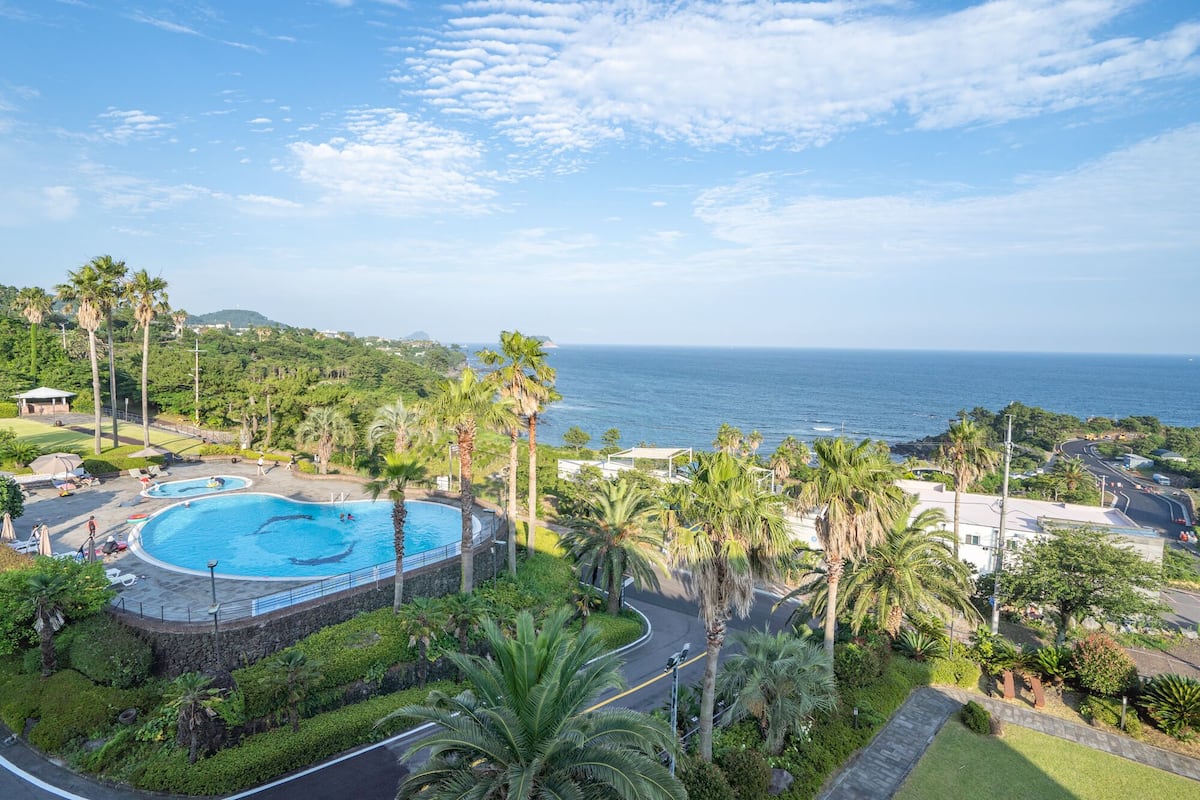 A resort with a large swimming pool, lush greenery, and a view of the ocean.