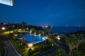 A resort with a swimming pool surrounded by palm trees and a view of the ocean at night. - Seaore Resort (Seogwipo)