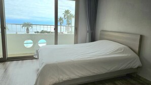 A hotel room with a bed, a view of the beach, and a balcony with a railing. - Seaore Resort (Seogwipo)