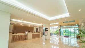 A spacious lobby with a reception desk, a glass entrance, and a view of greenery outside. - Seaore Resort (Seogwipo)