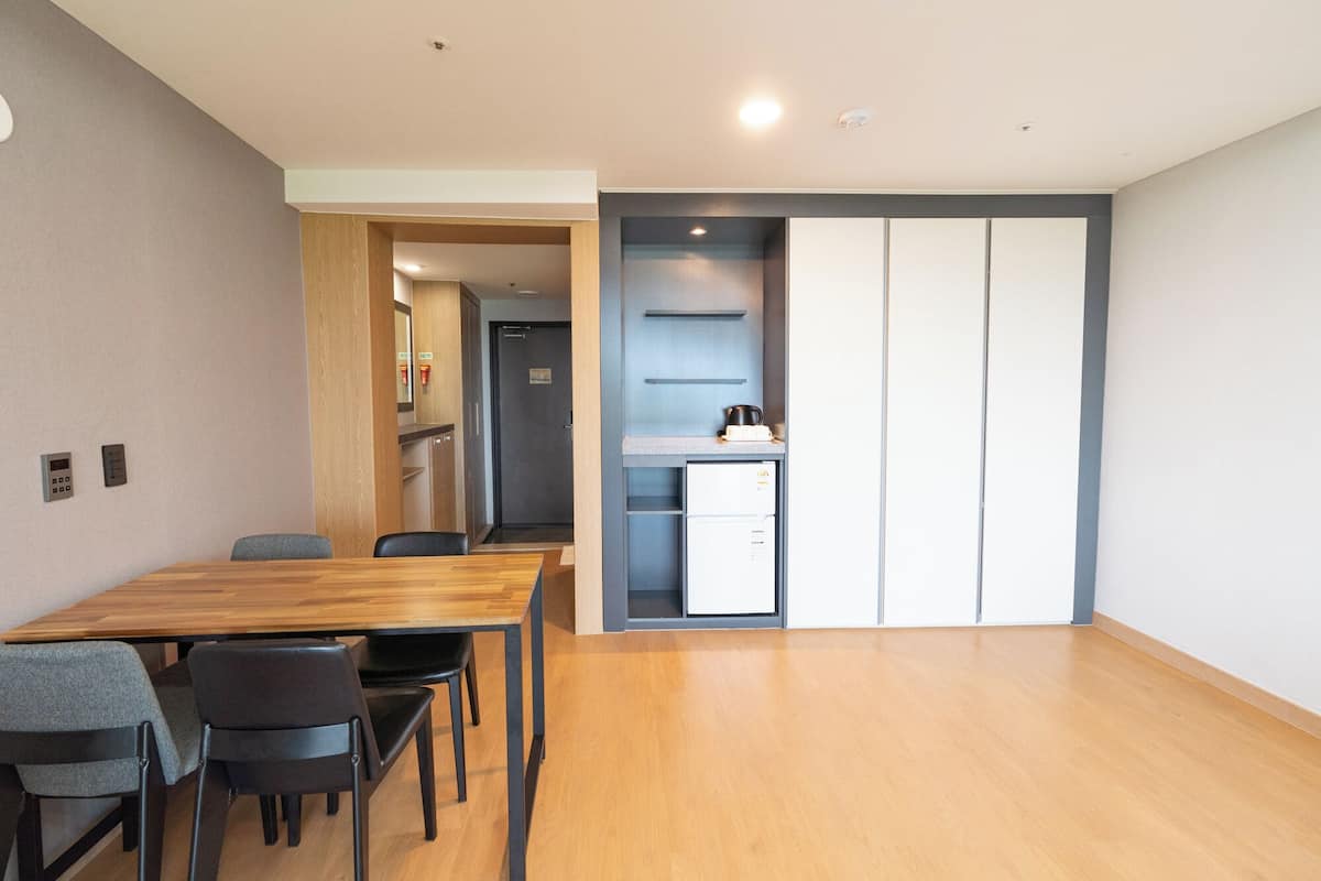 A modern hotel room with a wooden dining table, black chairs, a kitchenette, and a sliding door closet.