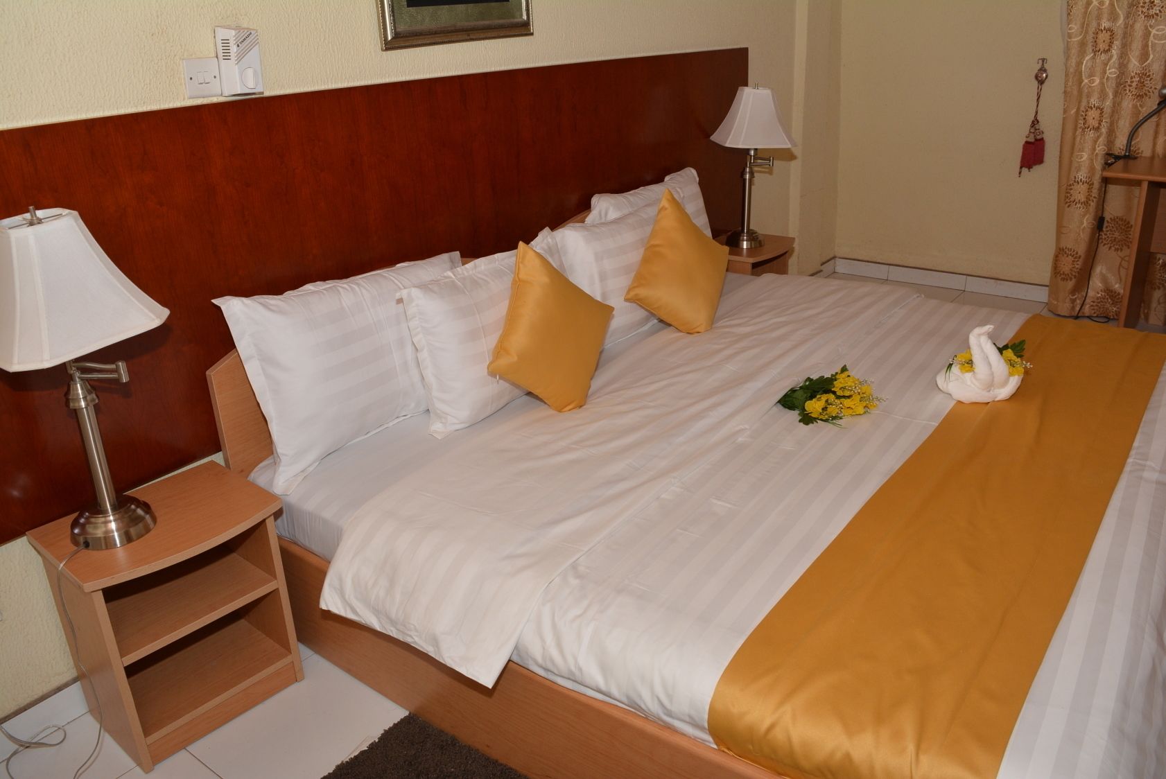 A neatly made bed with white and gold bedding, two bedside lamps, and a swan decoration on the bed.