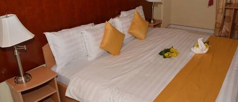 A neatly made bed with white and gold bedding, two bedside lamps, and a swan decoration on the bed.