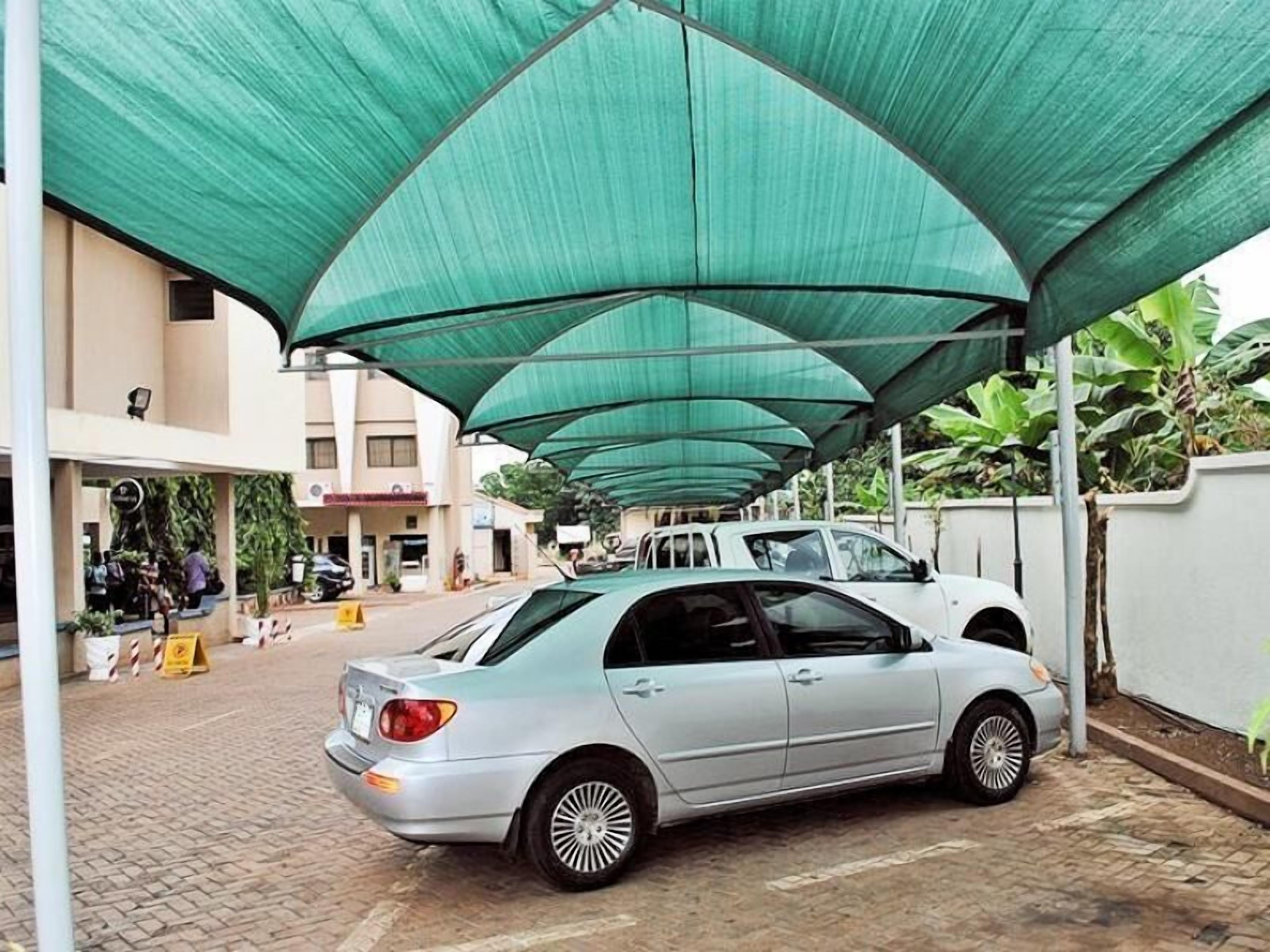 A silver car parked under a green canopy in a parking lot.