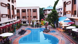 A swimming pool with lounge chairs and umbrellas, surrounded by buildings with air conditioning units. - Eusbett Hotel (Sunyani)