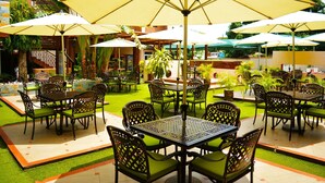 An outdoor patio with multiple tables and chairs, surrounded by greenery and umbrellas. - Eusbett Hotel (Sunyani)