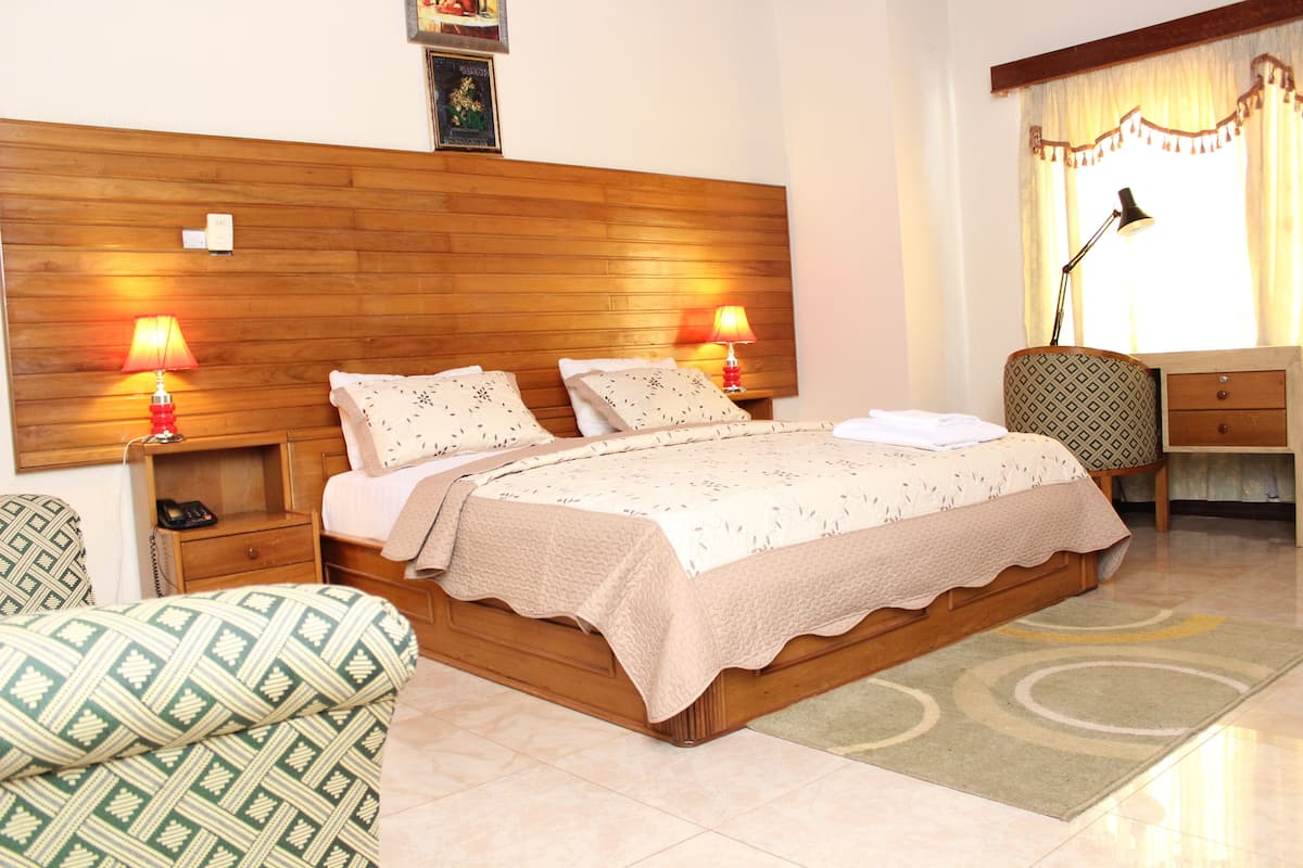 Une chambre à coucher bien rangée, avec une tête de lit en bois, deux lampes de chevet, une couvre-lit à motifs et une table de chevet avec une lampe.