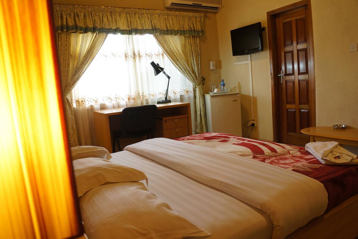 Une chambre d’hôtel équipée d’un lit, d’un bureau, d’une chaise et d’un téléviseur fixé au mur.