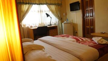 Una camera d'albergo con un letto, una scrivania, una sedia e un televisore montato a parete.