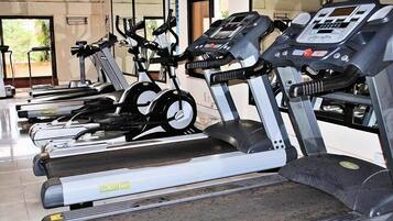 A row of stationary exercise bikes in a gym with a mirrored wall and a window in the background.