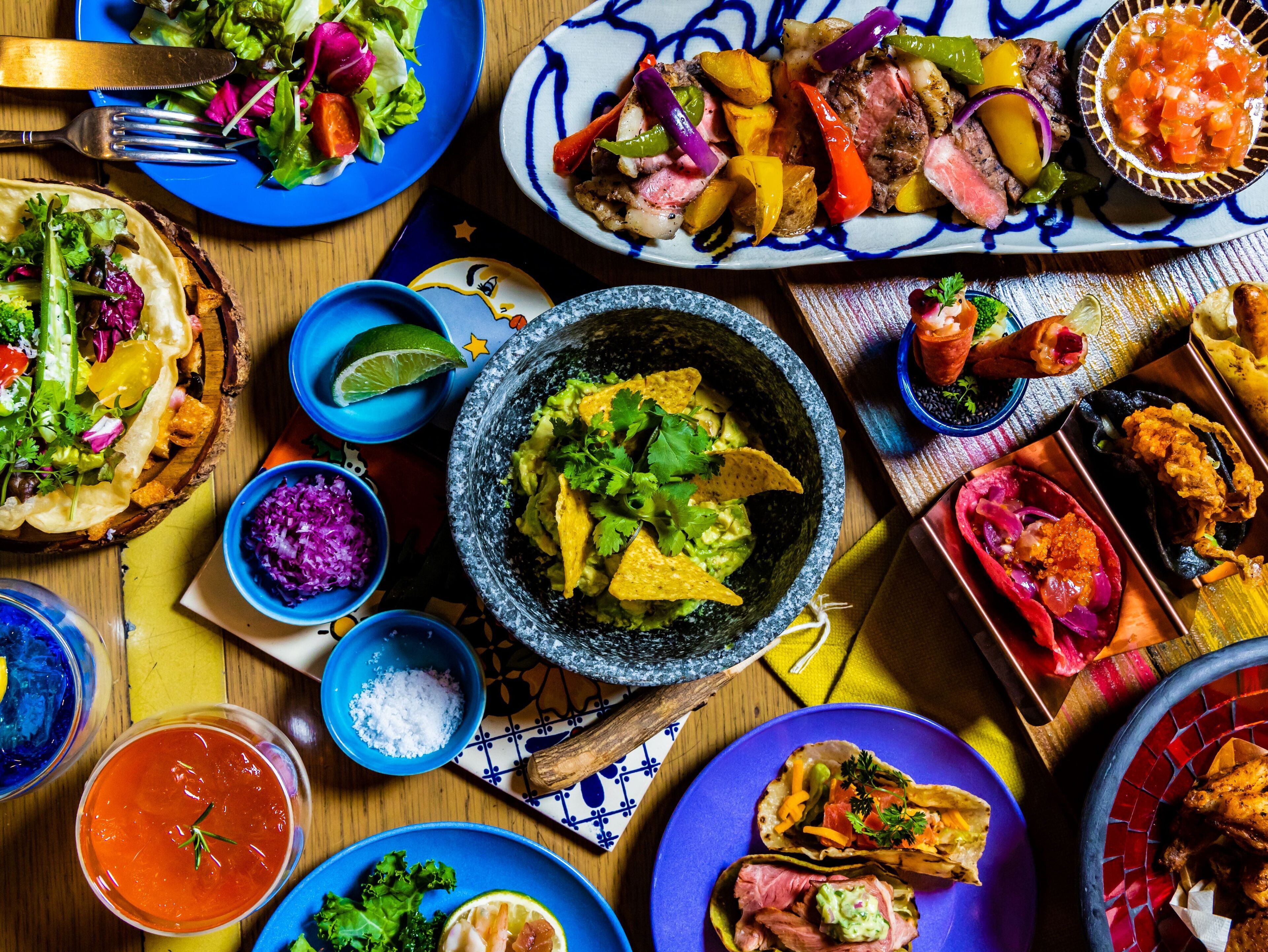 Variedad de platillos, incluyendo tacos, un tazón de guacamole y un plato de carne con verduras.