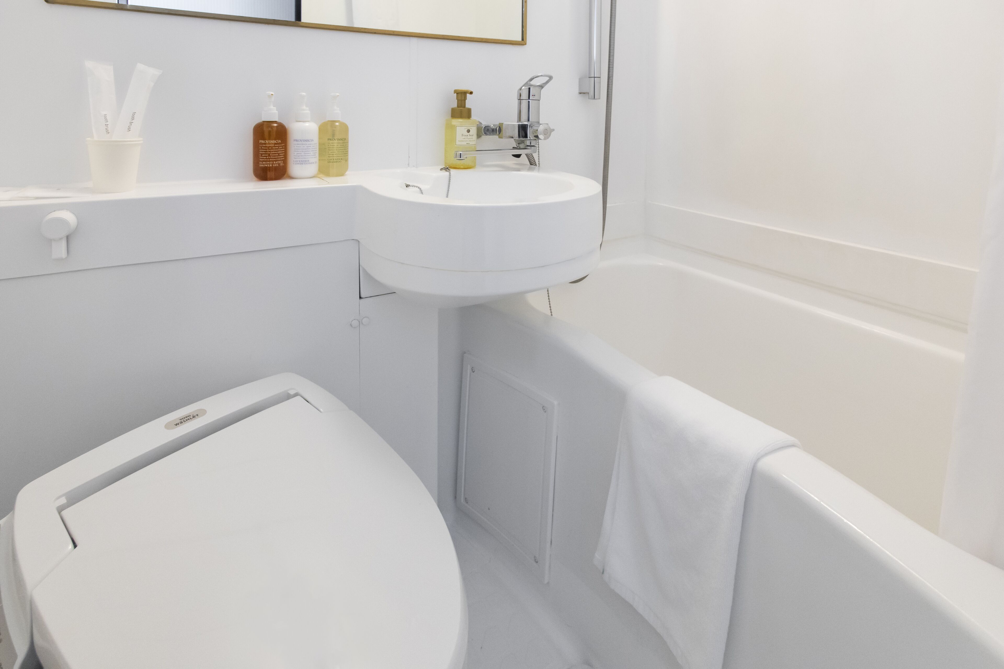 A bathroom with a white sink, toilet, and bathtub. There are toiletries on the sink counter.