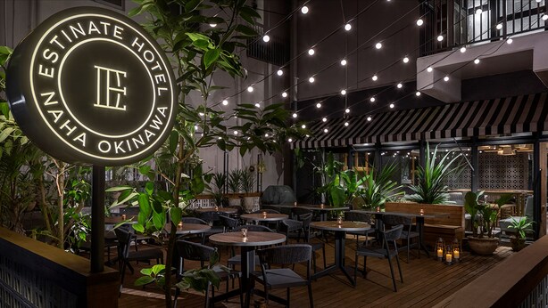An indoor dining area with round tables and chairs, surrounded by potted plants and string lights. - Estinate Hotel Naha (Naha)