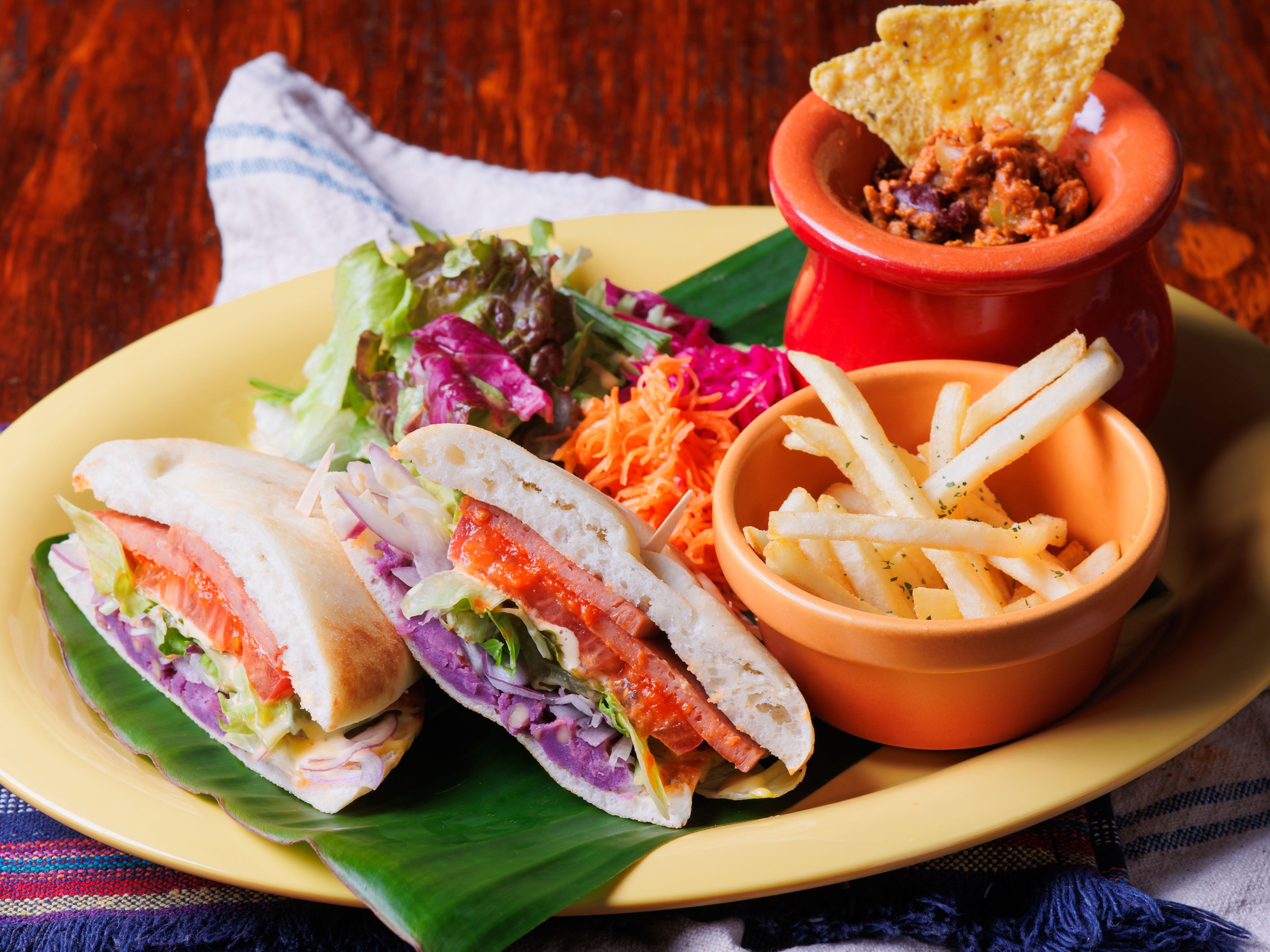 A plate with a sandwich cut in half, a bowl of fries, a small bowl of sauce, and a side salad.