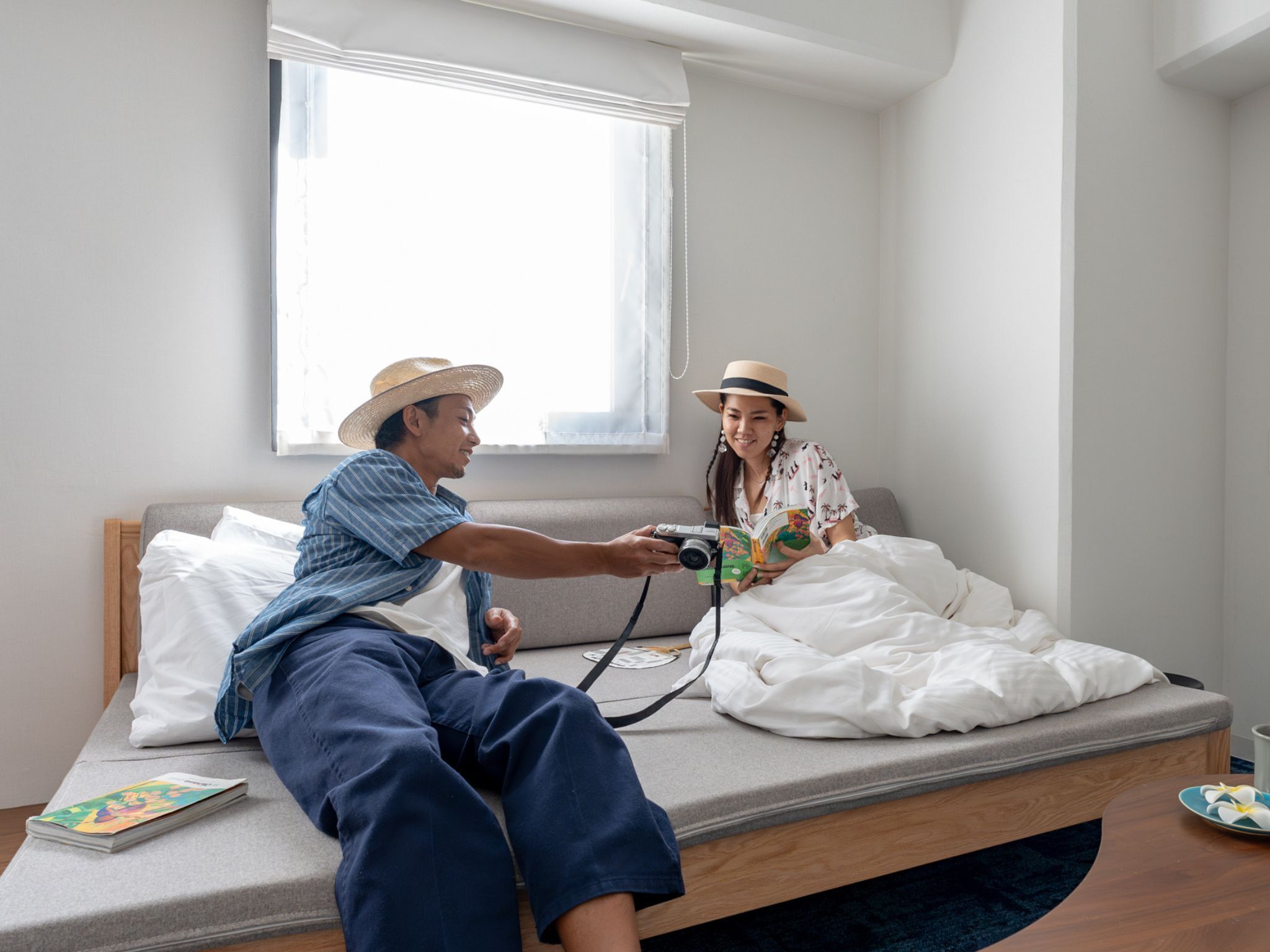 Ein Schlafzimmer mit einem Bett, einem Fenster und einem Nachttisch mit einem Buch und einer Kamera.