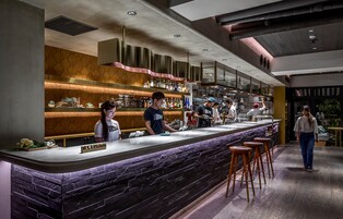 Uma área de bar moderna com bancada de mármore, banquetes de madeira e uma variedade de garrafas nas prateleiras.