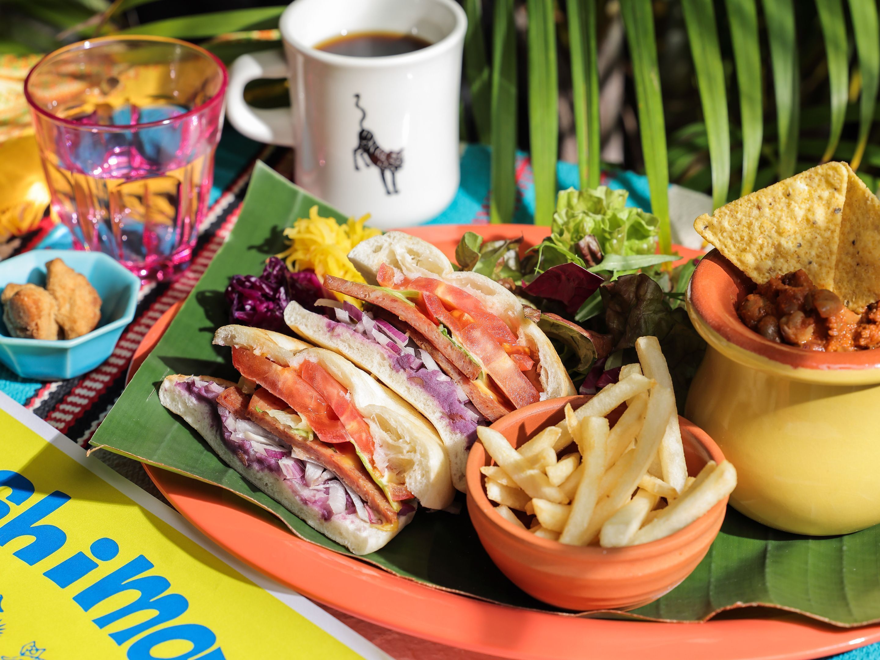 A meal with sandwiches, fries, and a cup of coffee on a colorful table.