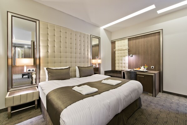 A modern hotel room with a large bed, a bedside table with a lamp, a dresser, and a large mirror. - Hotel Congress Avenue (Vilnius)