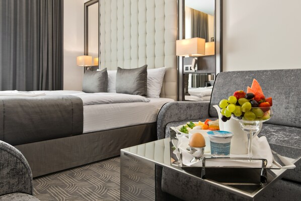 A hotel room with a bed, a sofa, a tray with fruit and a drink, and a lamp. - Hotel Congress Avenue (Vilnius)