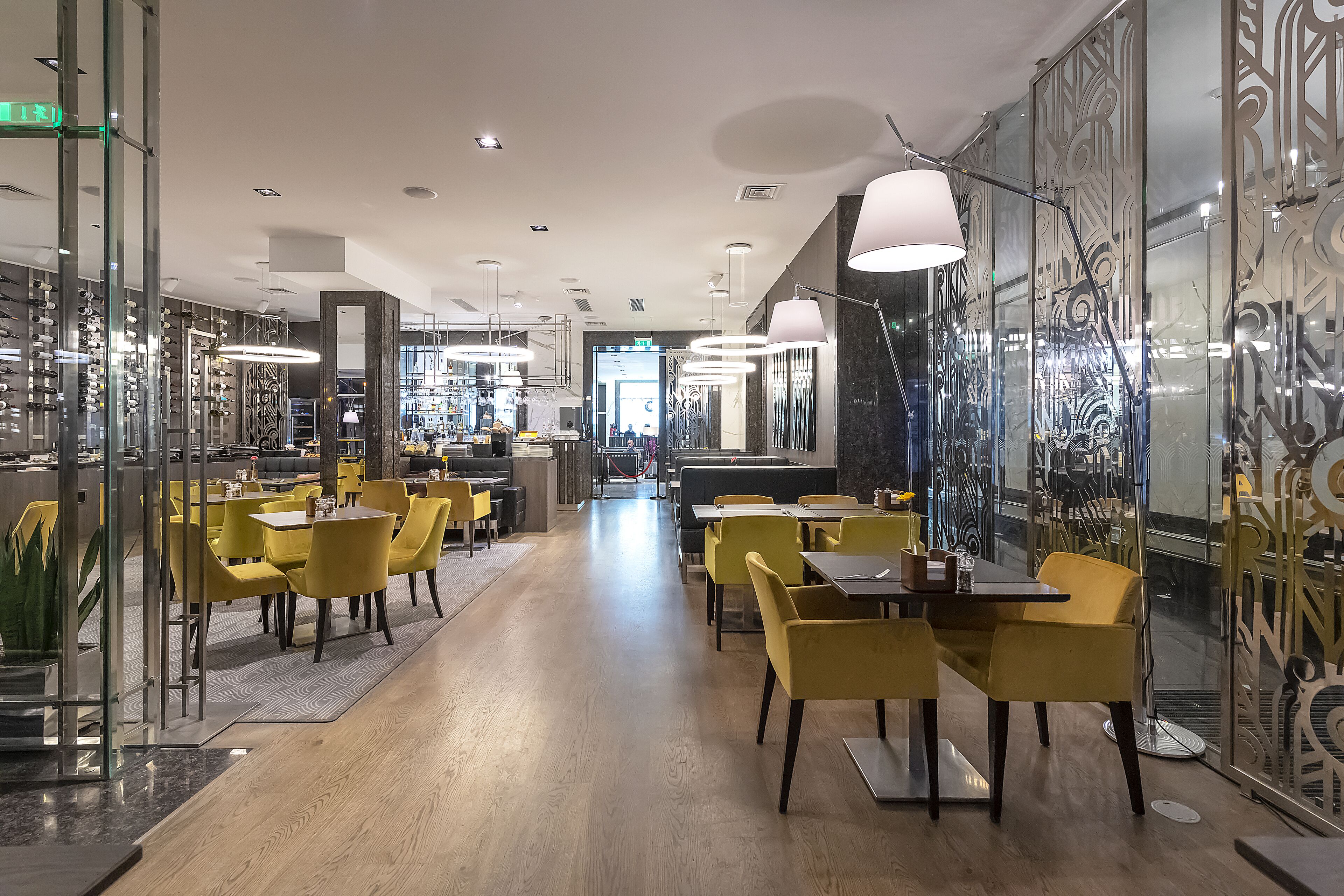 A modern restaurant with yellow chairs and tables, a bar area, and decorative wall panels.